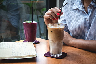 Woman drinking iced latte in cafe with notebook