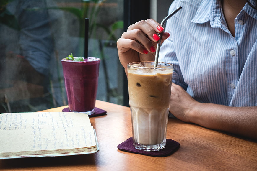 Woman drinking iced latte in cafe with notebook