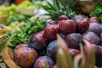 Fresh ripe plums in a wooden bowl at a farmers market