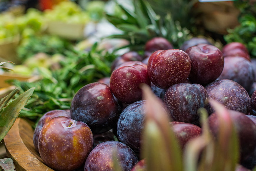 Fresh ripe plums in a wooden bowl at a farmers market