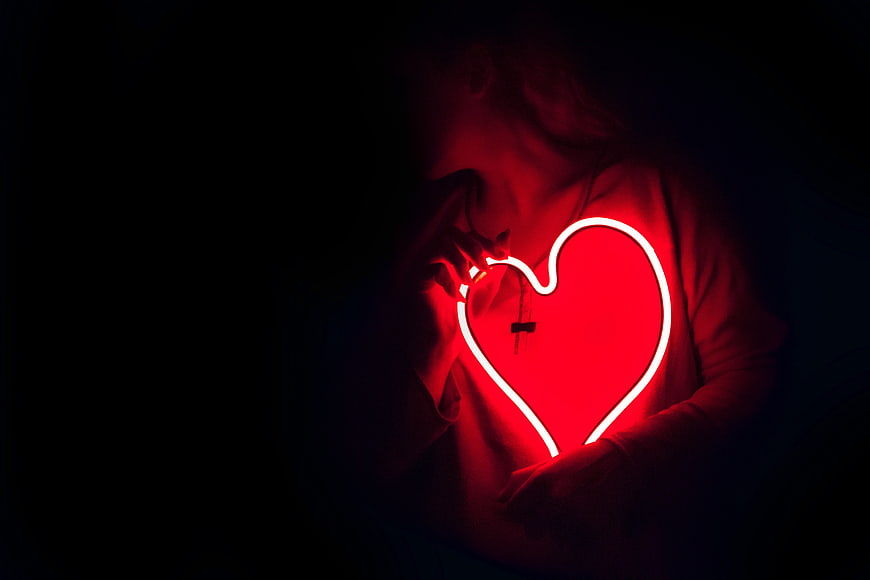 Woman holding glowing red neon heart in dark room