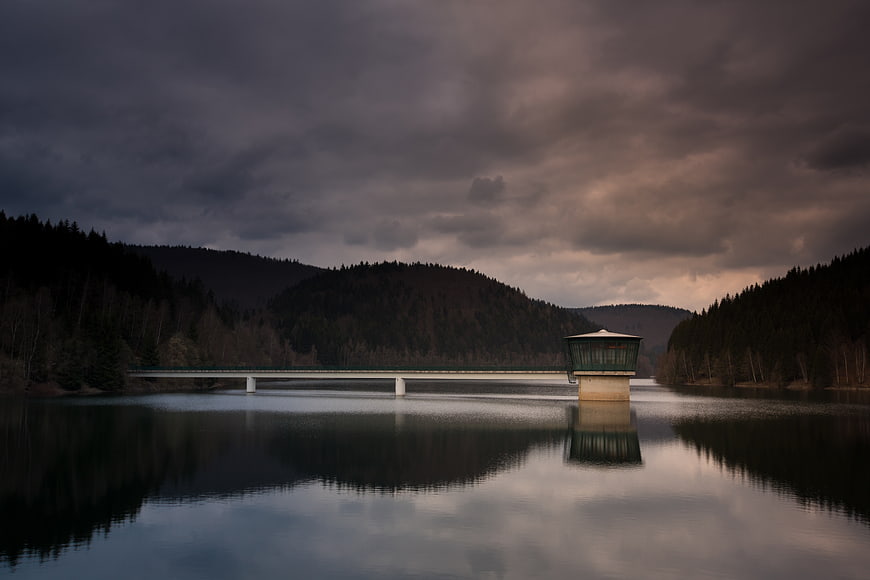 Dramatic Reservoir Bridge with Tower Under Stormy Sky