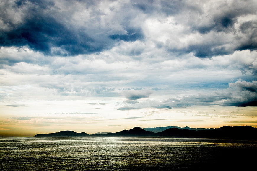 Dramatic cloudy sunset over ocean with distant mountain silhouette