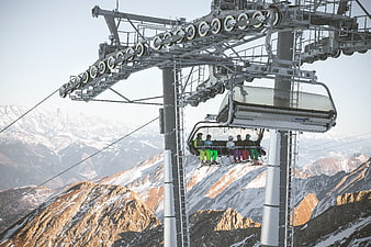 Ski lift chair with skiers against snowy mountain peaks