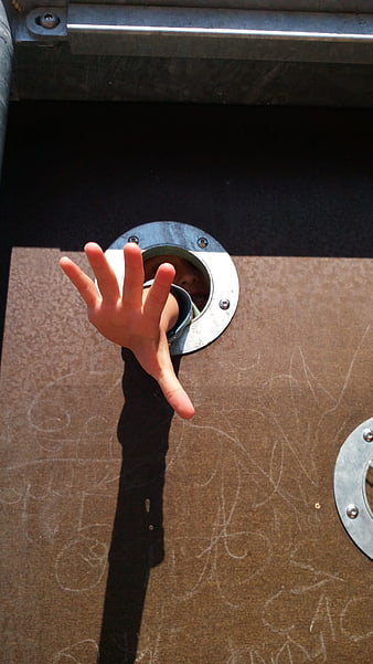 Child's hand reaching through playground climbing structure hole