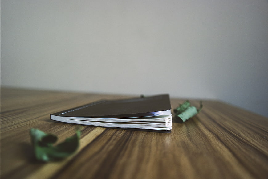 Minimalist black notebook on wooden table with leaves