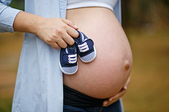 Pregnant Woman Holding Baby Shoes Against Belly