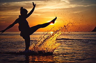 Silhouette of Woman Kicking Water at Sunset