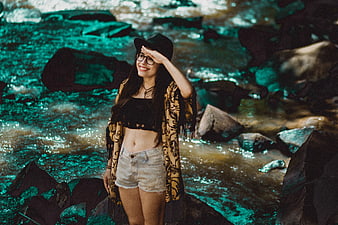 Happy woman in hat and glasses standing by river