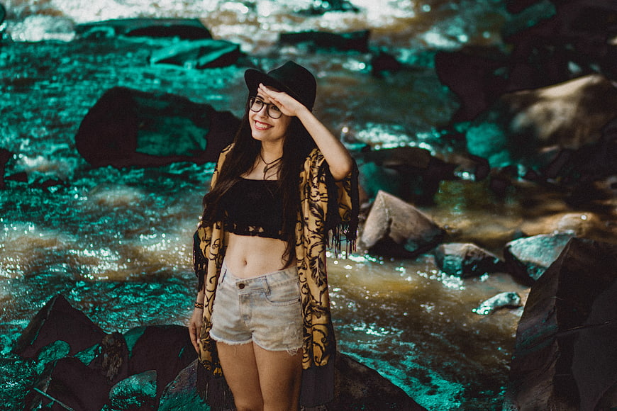 Happy woman in hat and glasses standing by river
