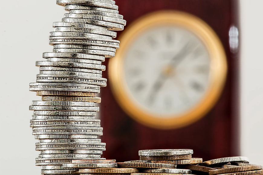 Stack of coins with blurred clock background