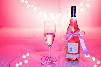 Pink wine bottle and glass with ribbon on festive background