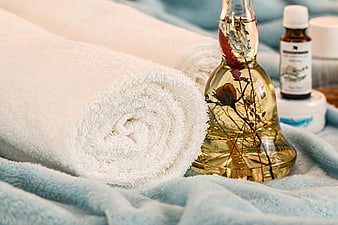 Rolled white towels and essential oil bottle on blue spa blanket