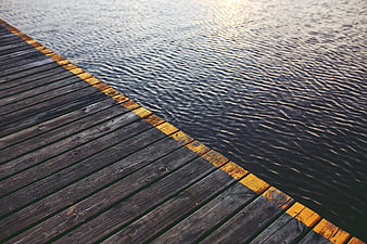 Wooden pier edge with yellow safety line on calm water