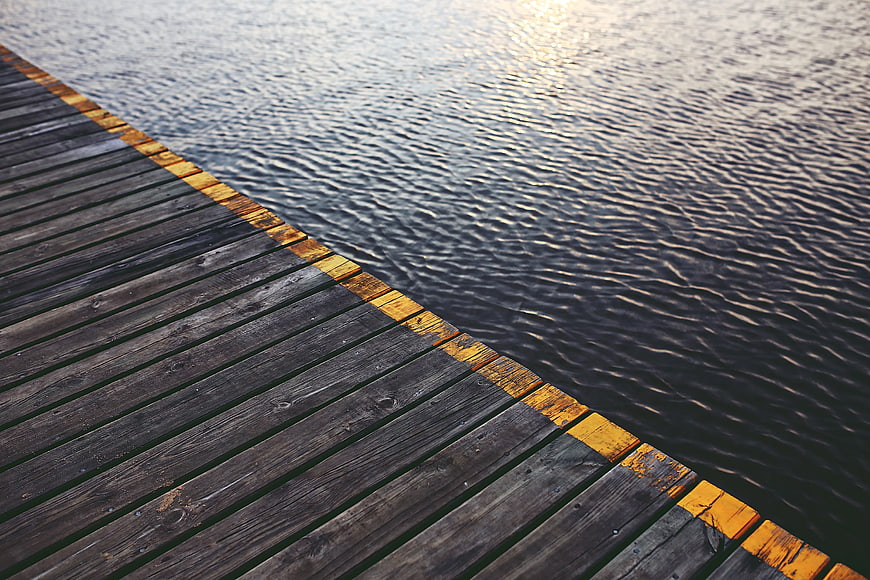 Wooden pier edge with yellow safety line on calm water