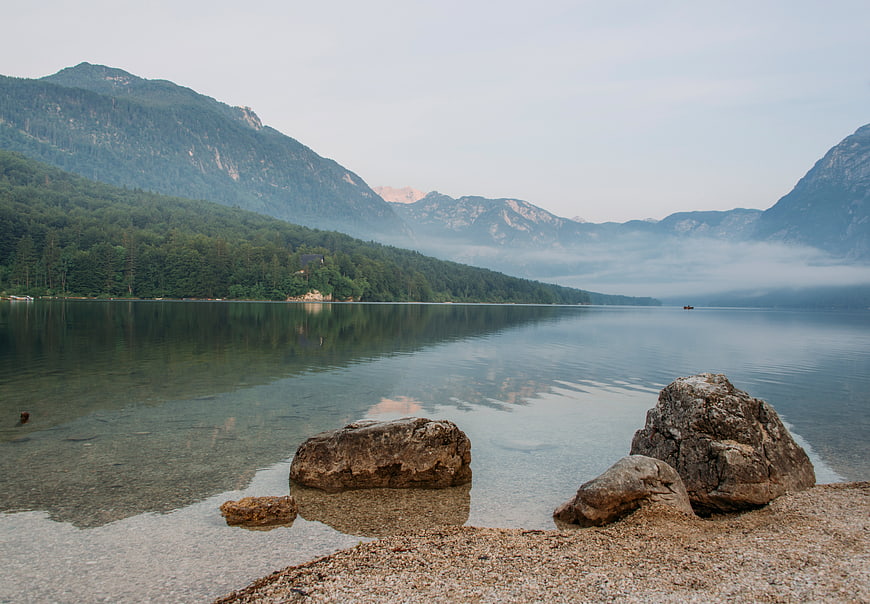 Serene Mountain Lake Landscape with Misty Reflections and Foreground Rocks