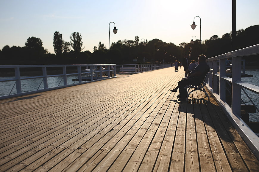 Man sitting on bench on wooden pier at sunset