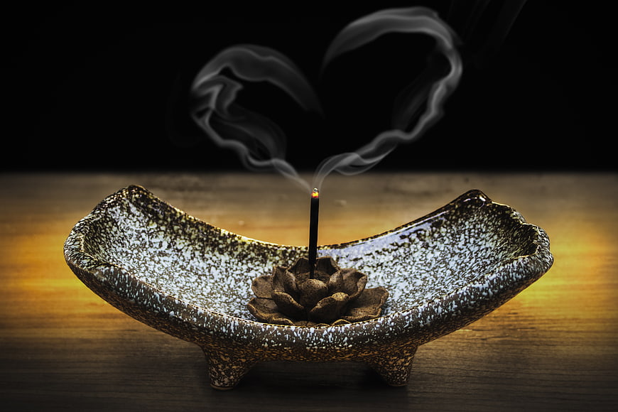 Incense smoke forming heart shape in ceramic bowl