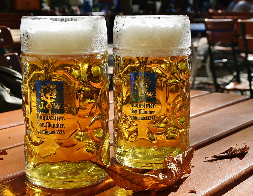 Two Augustiner beer mugs with foam on a wooden table