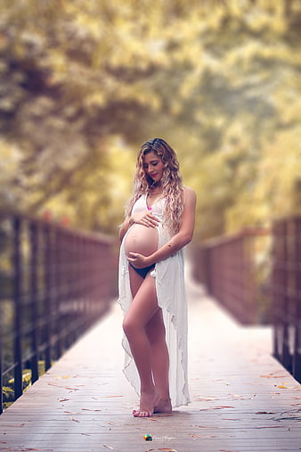 Pregnant woman holding belly on wooden bridge