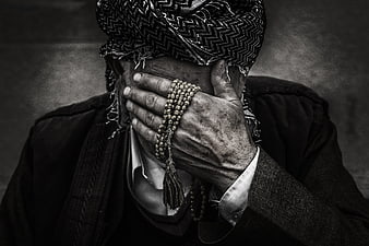 Elderly man hiding face with prayer beads in black and white