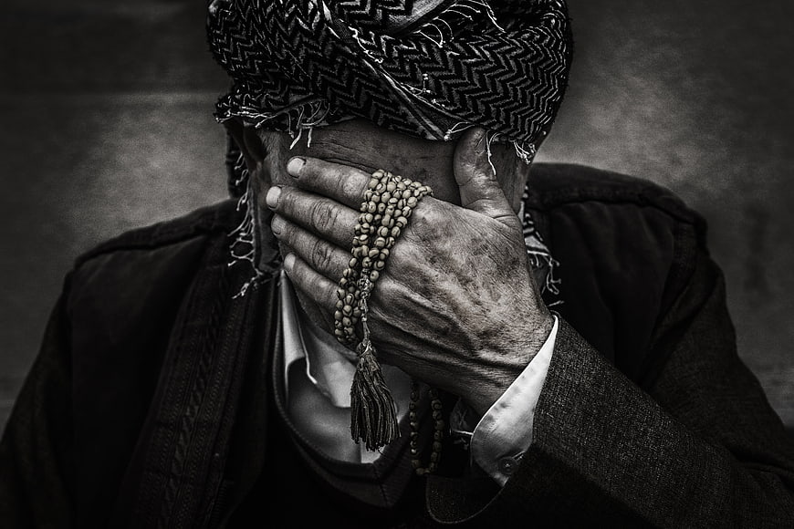 Elderly man hiding face with prayer beads in black and white