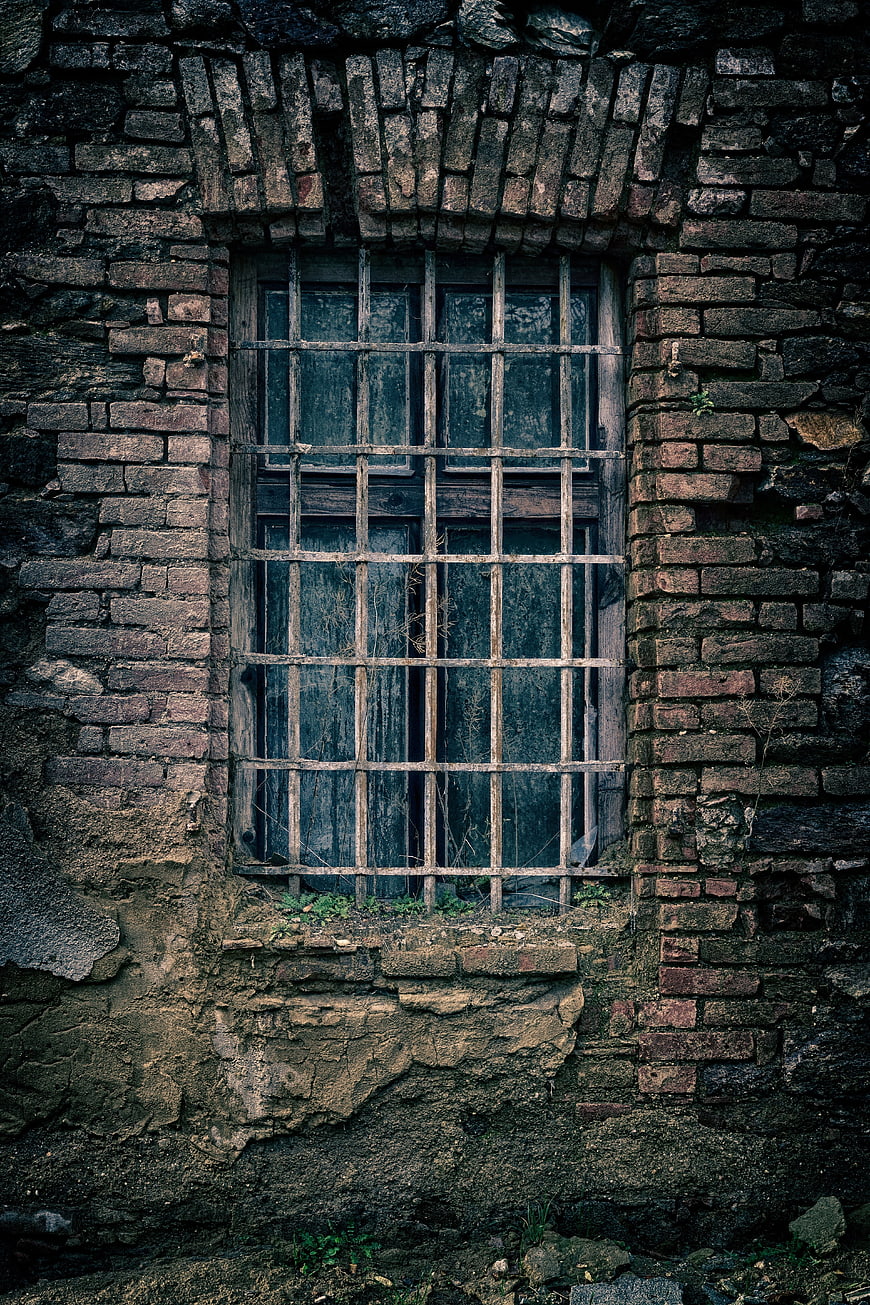 Old barred window in weathered brick wall