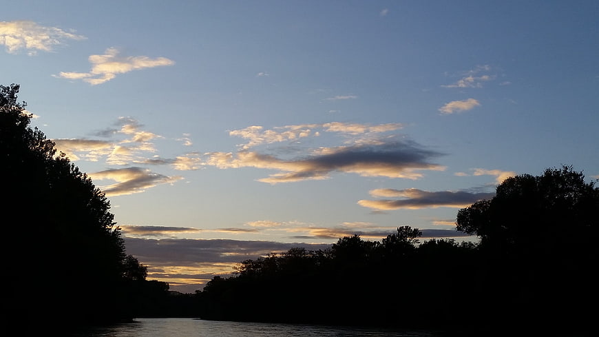 River Landscape At Dusk With Silhouetted Trees And Clouds