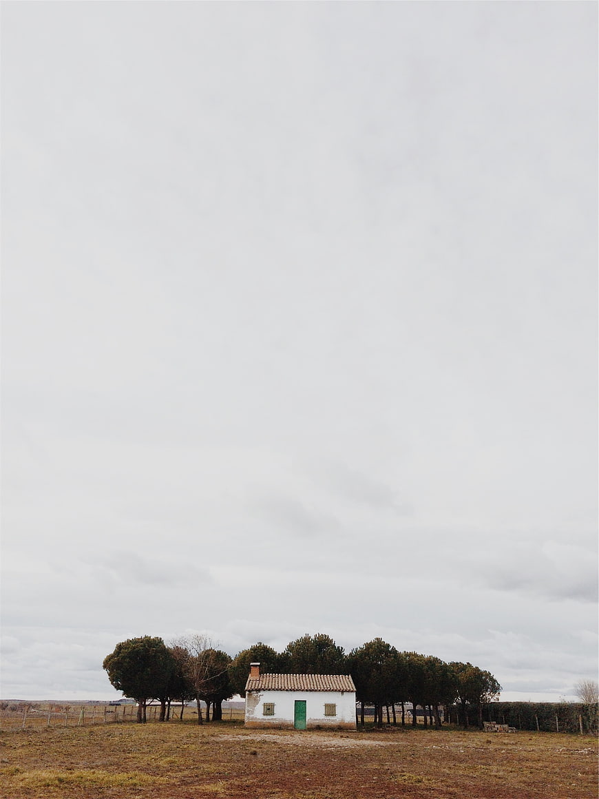 Small white rural house with green door under cloudy sky