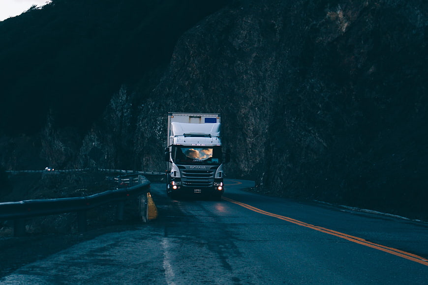 White Scania Truck Driving On Dark Mountain Road At Dusk