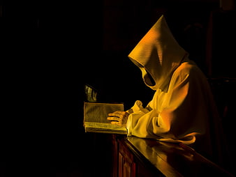 Monk in white hood reading book in dark church