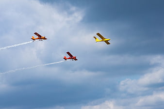 Three colorful biplanes performing aerobatics in blue sky
