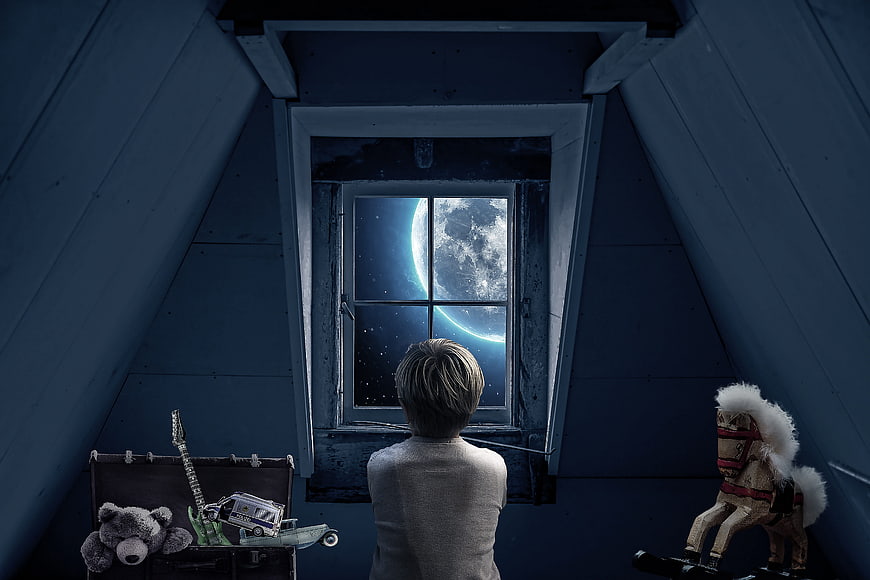 Boy looking at giant moon from attic window with toys
