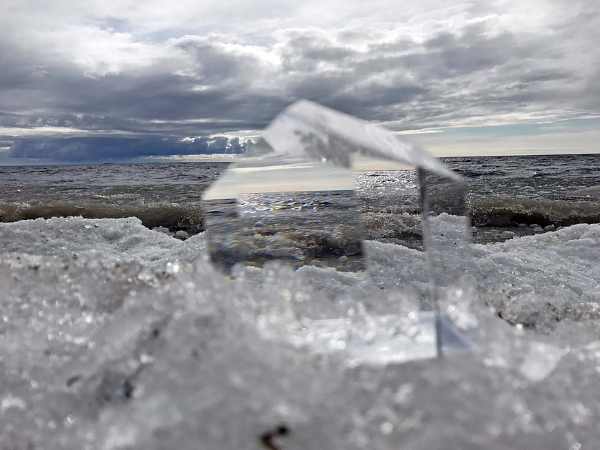 Transparent Ice Cube on Snowy Shore with Ocean Background
