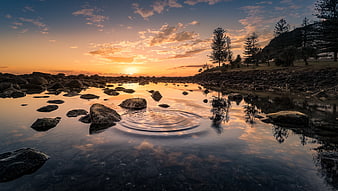 Serene Sunset Over Rocky Shore with Water Ripples and Reflections