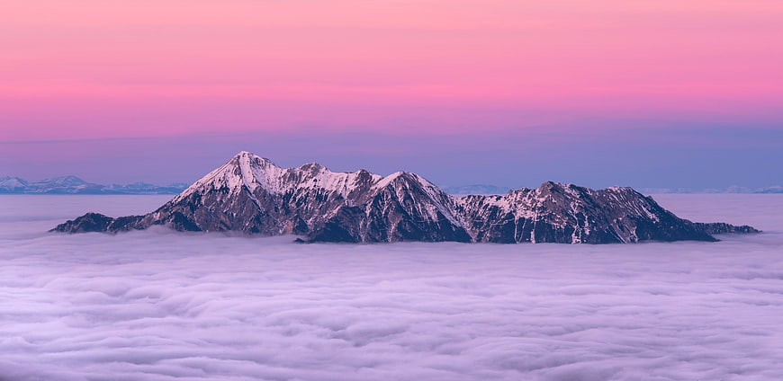 Snowy mountain peaks rising above sea of clouds at pink sunset