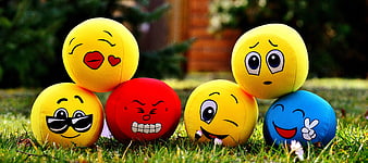 Colorful plush emoji balls on green grass