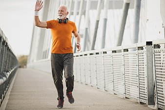 Active senior man jogging and waving on a bridge