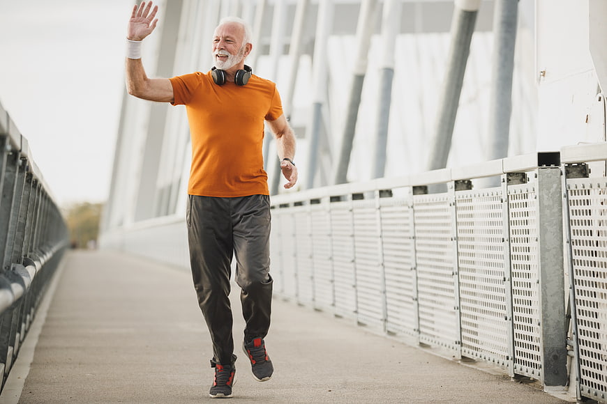 Active senior man jogging and waving on a bridge