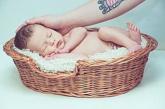 Sleeping newborn baby in wicker basket with father's hand