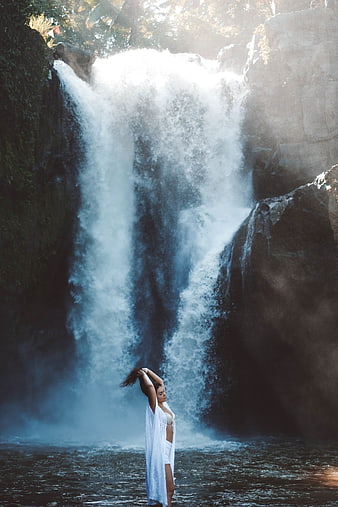 Woman in White Dress Standing in Front of Majestic Waterfall