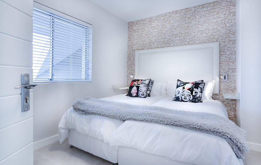 Modern Minimalist Bedroom With White Bedding And Exposed Brick Accent Wall