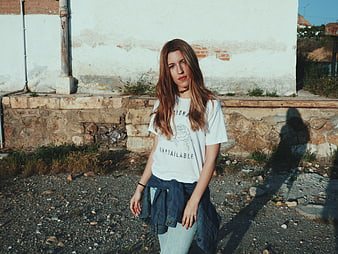 Young woman in white t-shirt standing against rustic wall