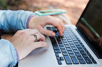 Close-up of hands typing on a silver laptop keyboard outdoors