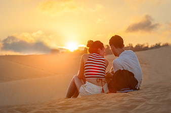 Romantic couple sitting on sand dunes watching sunset