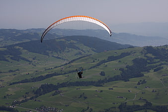 Paraglider soaring over green Swiss mountain landscape