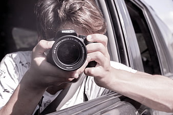 Young man taking a photo with a Canon camera from a car window