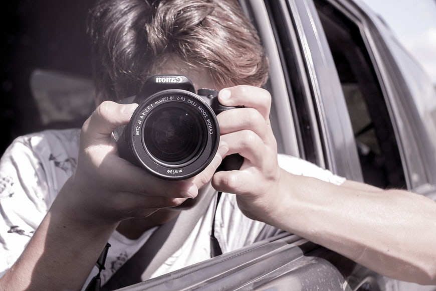 Young man taking a photo with a Canon camera from a car window