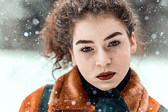 Close-up portrait of young woman with curly hair in winter snow