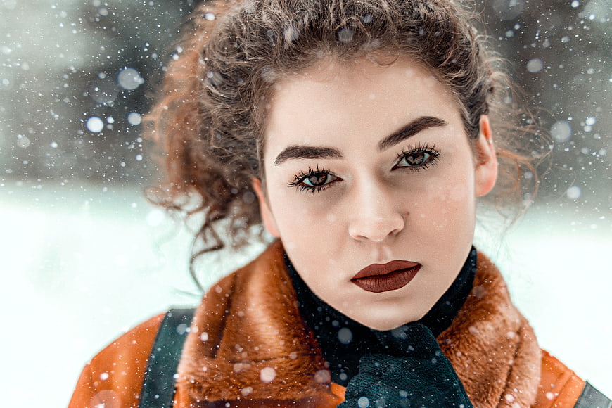 Close-up portrait of young woman with curly hair in winter snow
